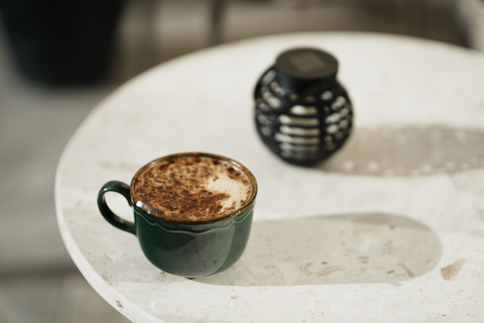 A cappuccino in a dark green cup on a white stone table in morning sun