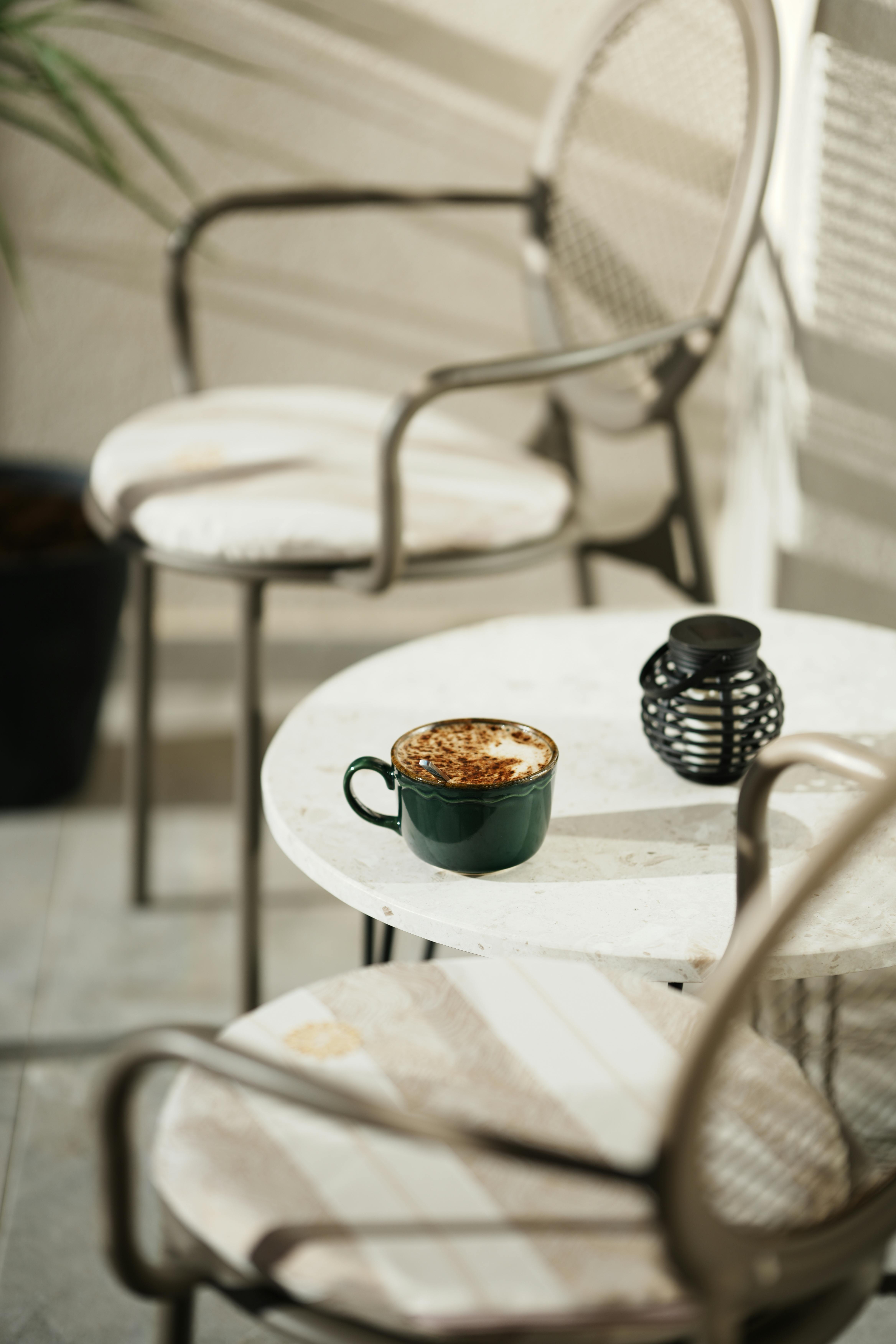 Sunlit balcony with coffee cup and wrought iron chairs, perfect for relaxation.