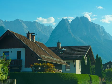A picturesque alpine village with traditional chalets framed by towering, rugged mountains under a bright blue sky.