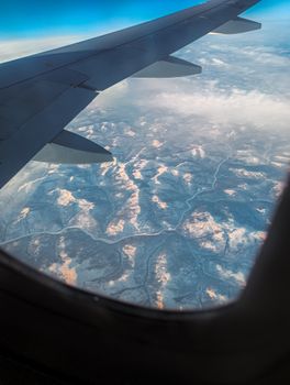 Stunning aerial view of snow-covered mountains captured from an airplane window, showcasing a serene winter scene.