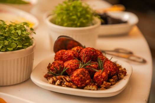 Close-up of spicy cheese balls garnished with rosemary and nuts, surrounded by fresh herbs.