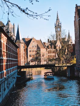 Scenic view of Ghent's historic architecture along the canal, featuring a classic Flemish clock tower.