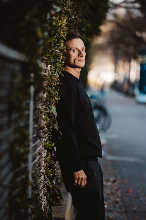 Free Casual portrait of a man leaning against a fence in Berlin, Germany outdoors. Stock Photo