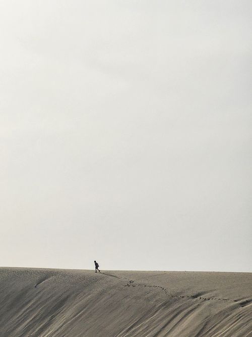 Free A lone person walking on expansive sand dunes under a clear sky. Stock Photo