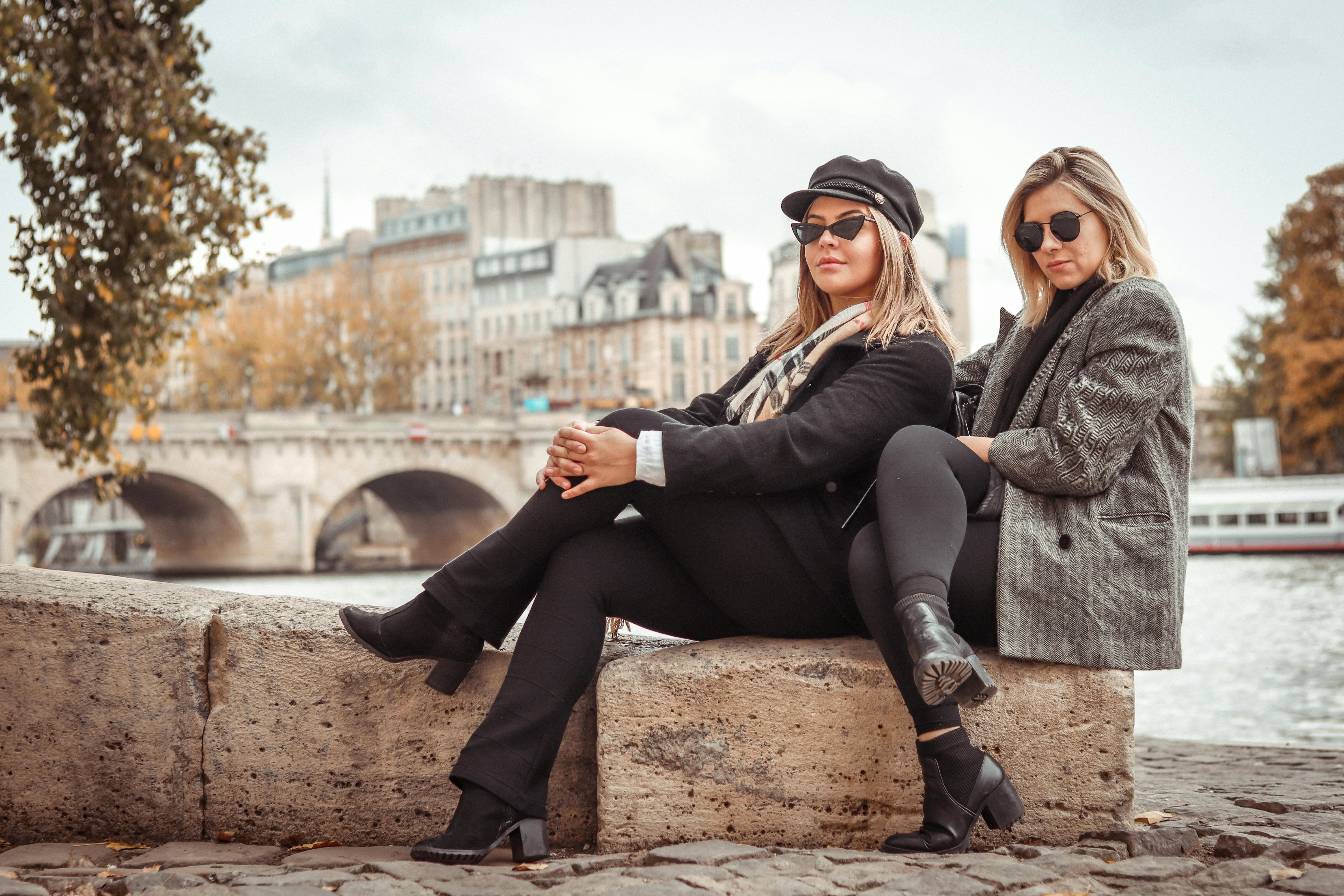 两位时尚女性坐在塞纳河边，身后是巴黎的建筑和秋叶