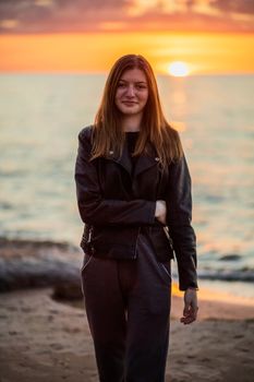 Smiling woman at beach sunrise, wearing a leather jacket. Calm and serene scene.