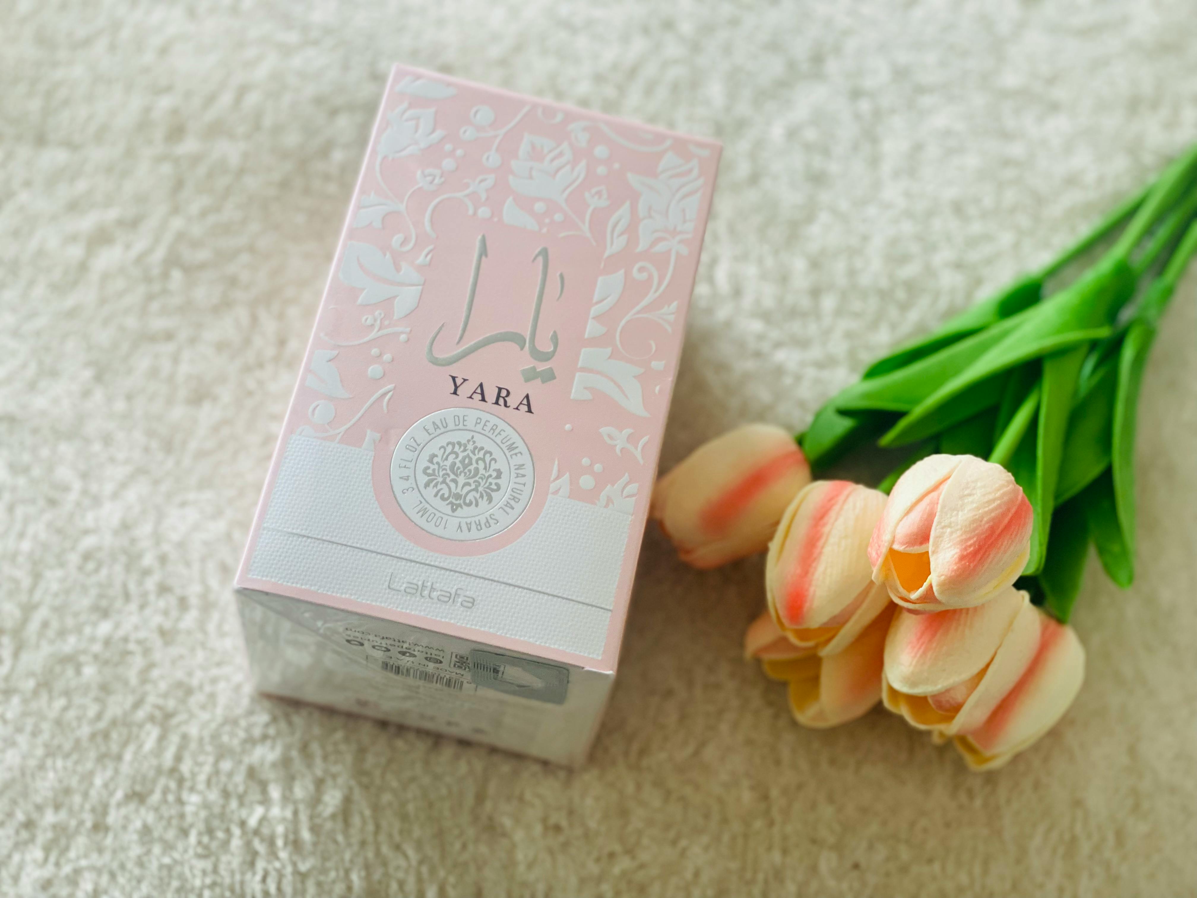 Yara perfume box alongside pink tulips placed on a plush carpet, showcasing elegance and freshness.