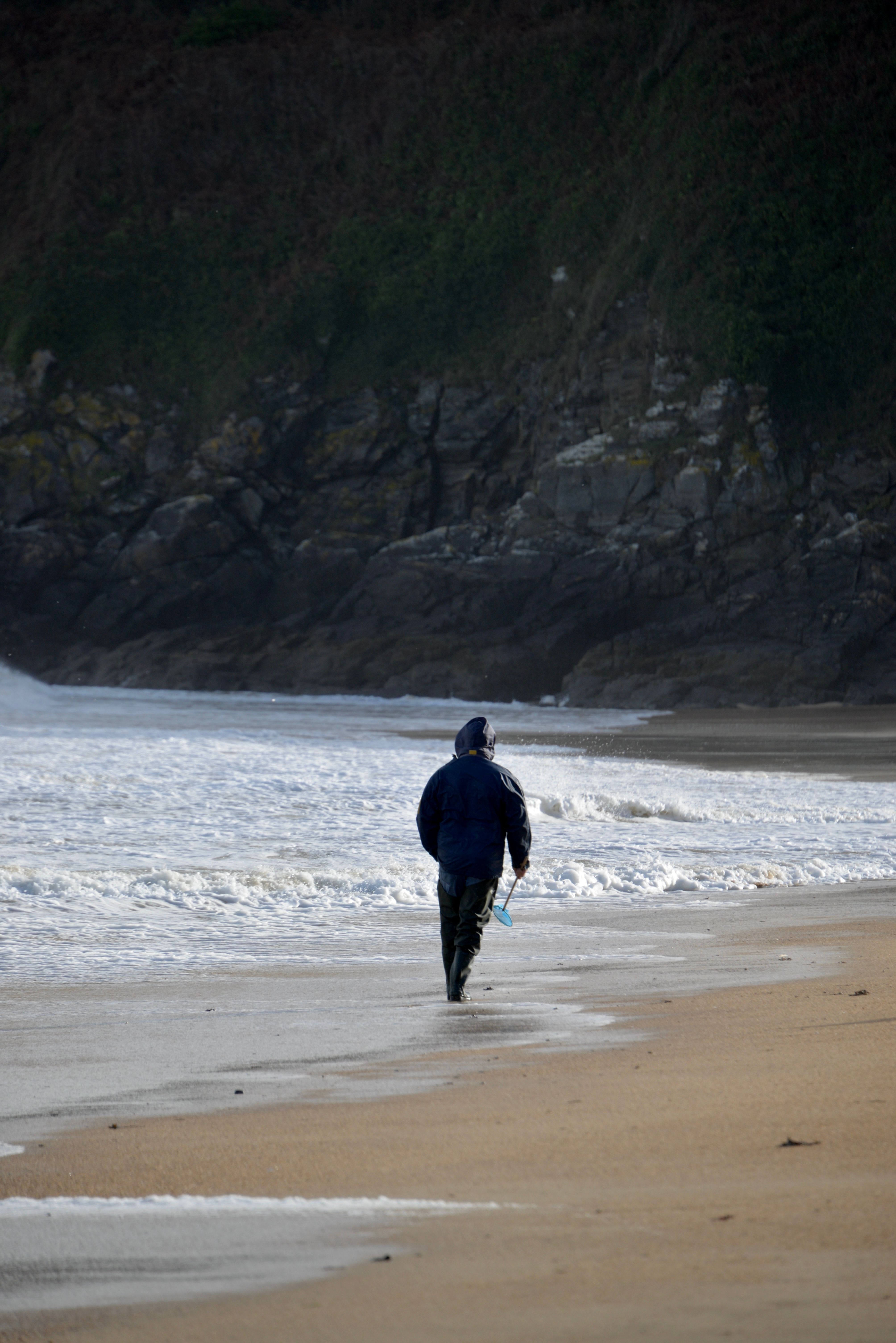 A solitary person walks along a tranquil winter beach, waves gently lapping at the shore.