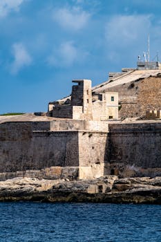 Ancient stone fortification along the coast in Valletta, Malta under a clear blue sky.