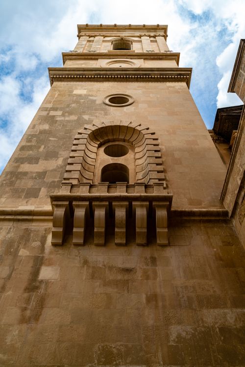 Free Tall beige stone tower with decorative arches against a blue sky in Valletta, Malta. Stock Photo