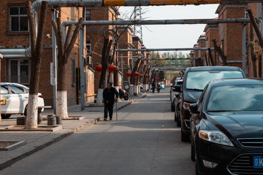 Street view of a suburban area featuring parked cars, brick buildings, and red lanterns.