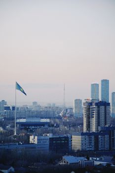 A scenic view of Astana skyline featuring the Kazakhstan flag prominently waving, highlighting the city's modern architecture.