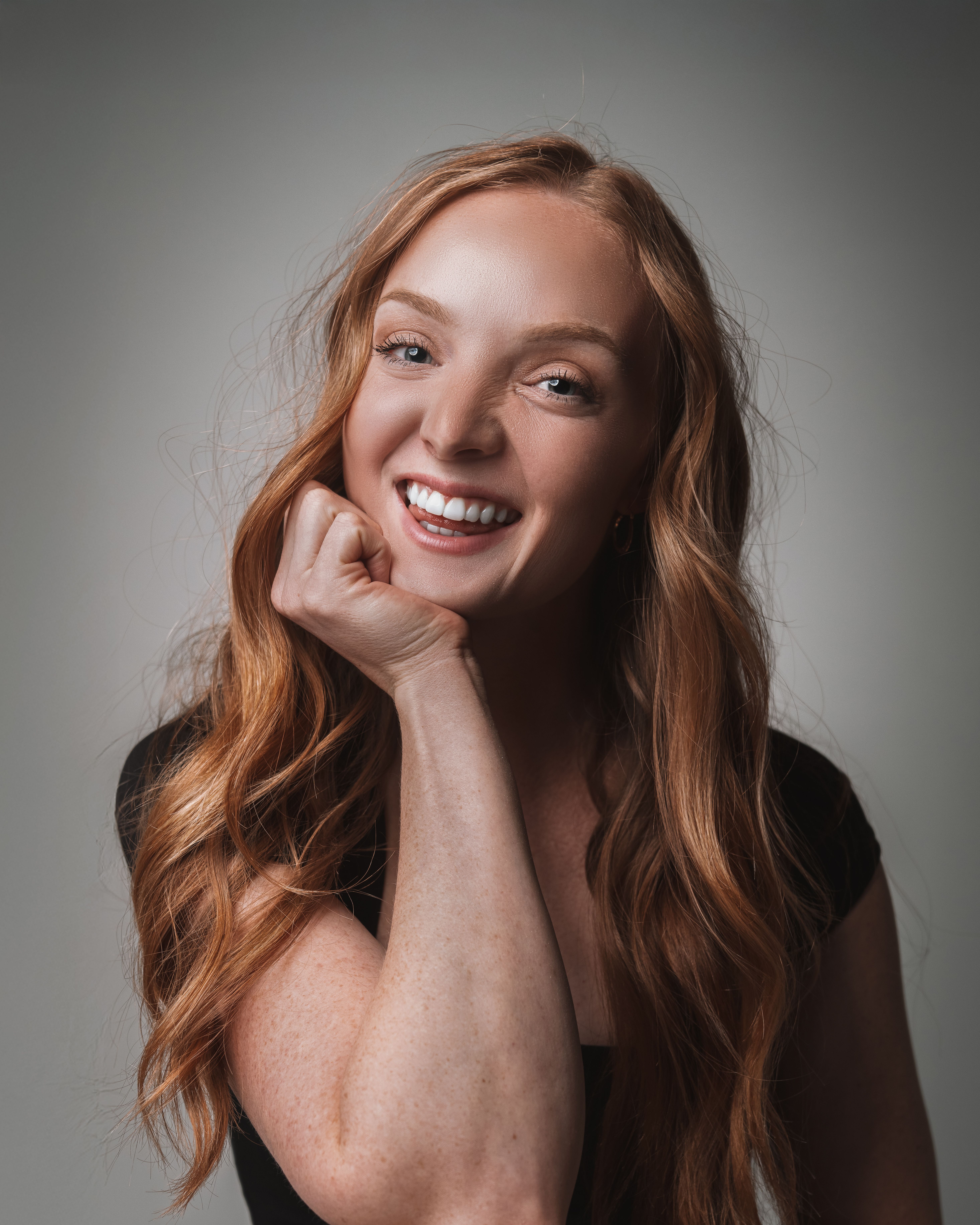 A close-up portrait of a smiling woman with long, ginger hair and a confident expression.