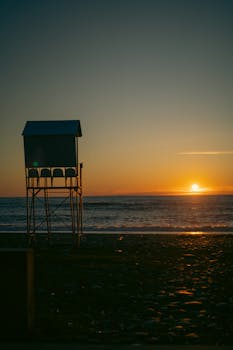 A serene beach sunset with silhouetted lifeguard tower and calm waves.