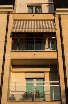 A modern building balcony featuring flower pots and a striped awning during daytime.
