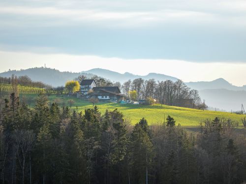 Free Charming rural scene of a homestead nestled in lush green hills with misty mountain backdrop. Stock Photo