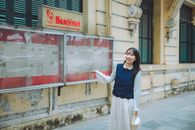 Young woman smiling in front of an outdoor newspaper display.