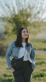 A woman in a denim jacket enjoys a sunny day outdoors in a natural setting.