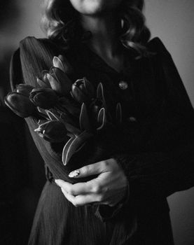 Moody black and white image of a woman holding tulips, exuding vintage elegance.