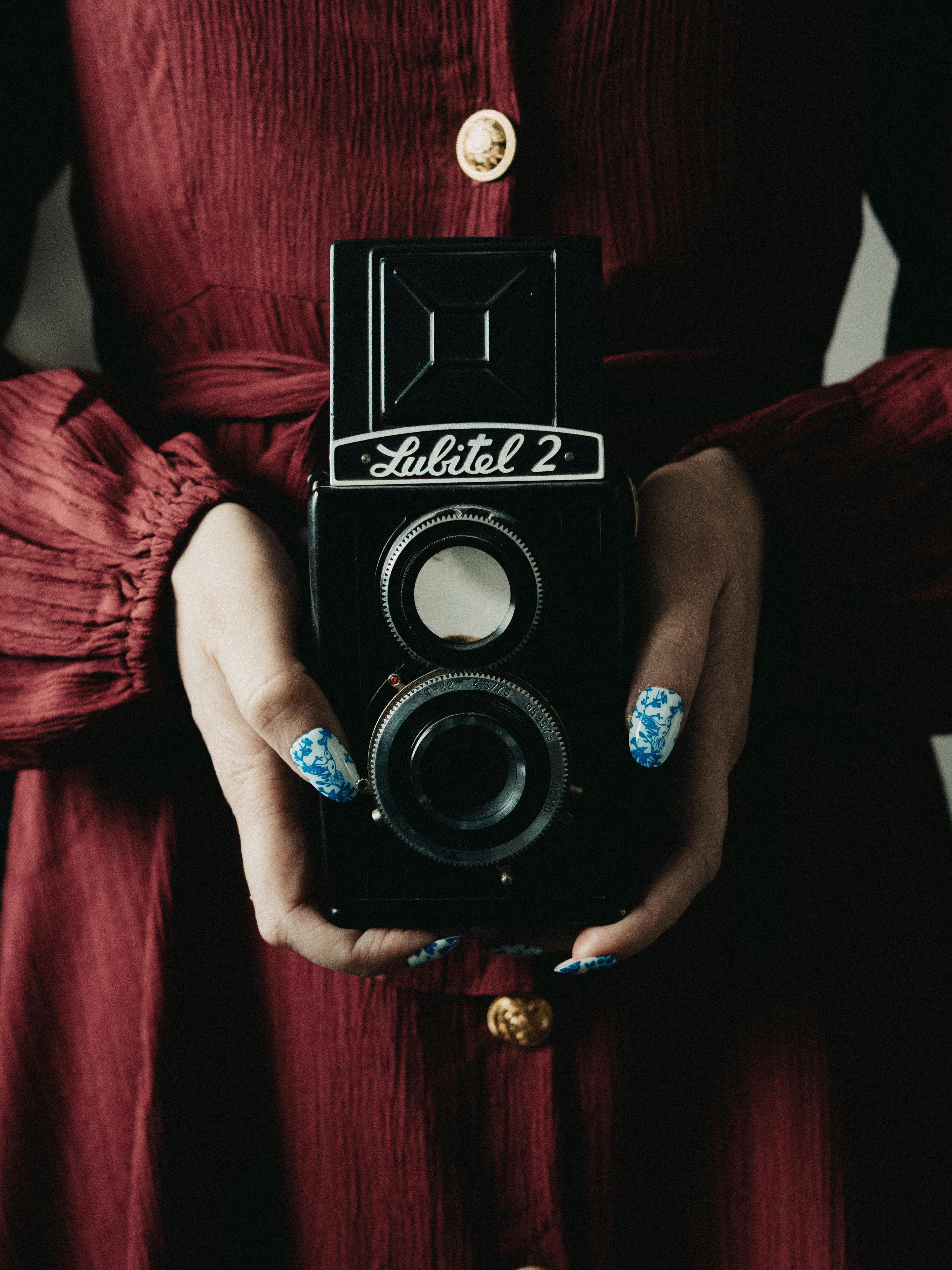 A woman wearing a red dress holds a vintage Lubitel 2 camera, emphasizing a retro aesthetic.