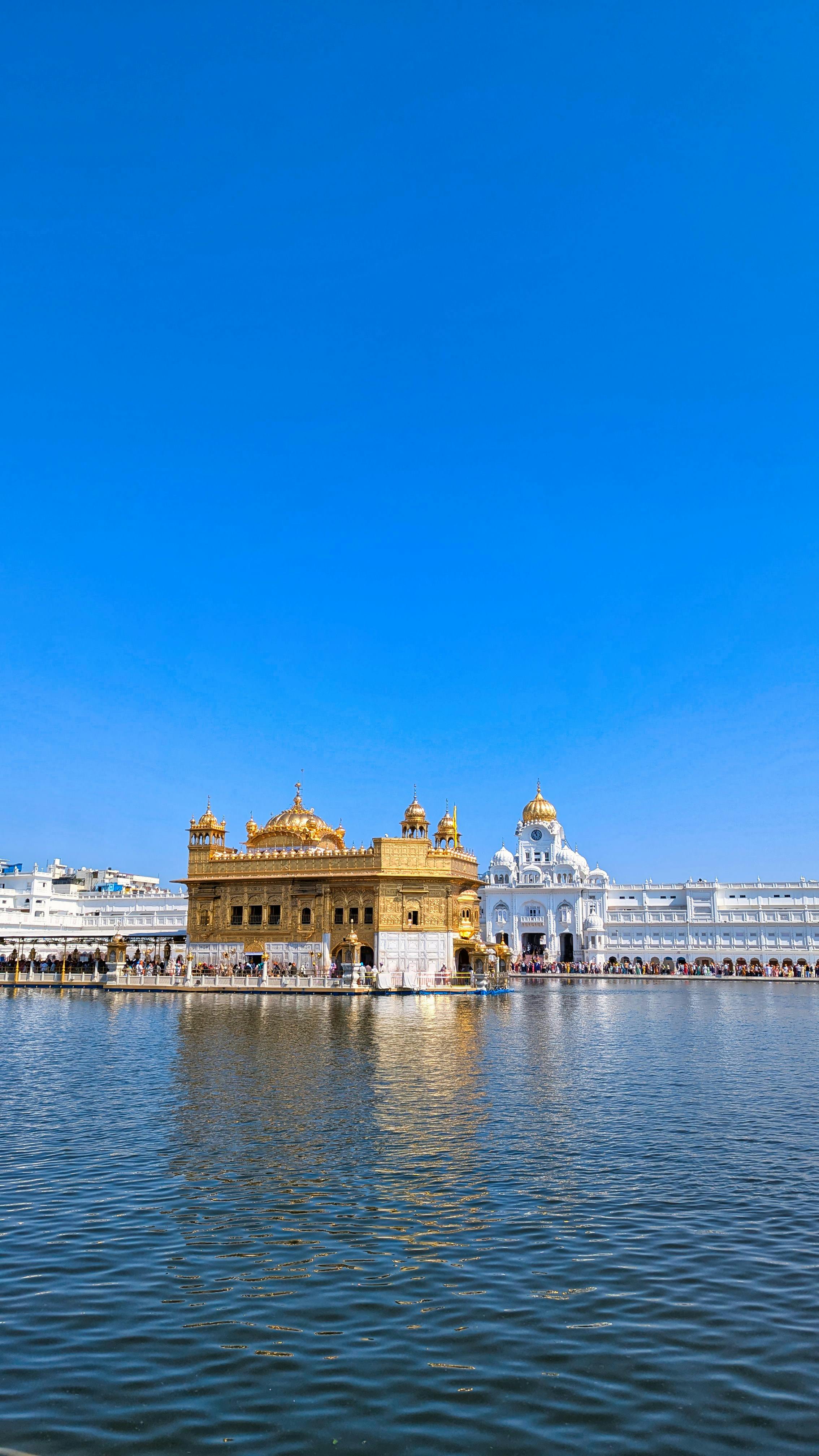 The stunning Golden Temple in Amritsar against a bright blue sky, reflecting in calm waters.