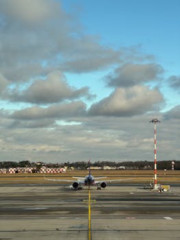 An airplane aligned on runway at a bustling airport under a cloudy sky.