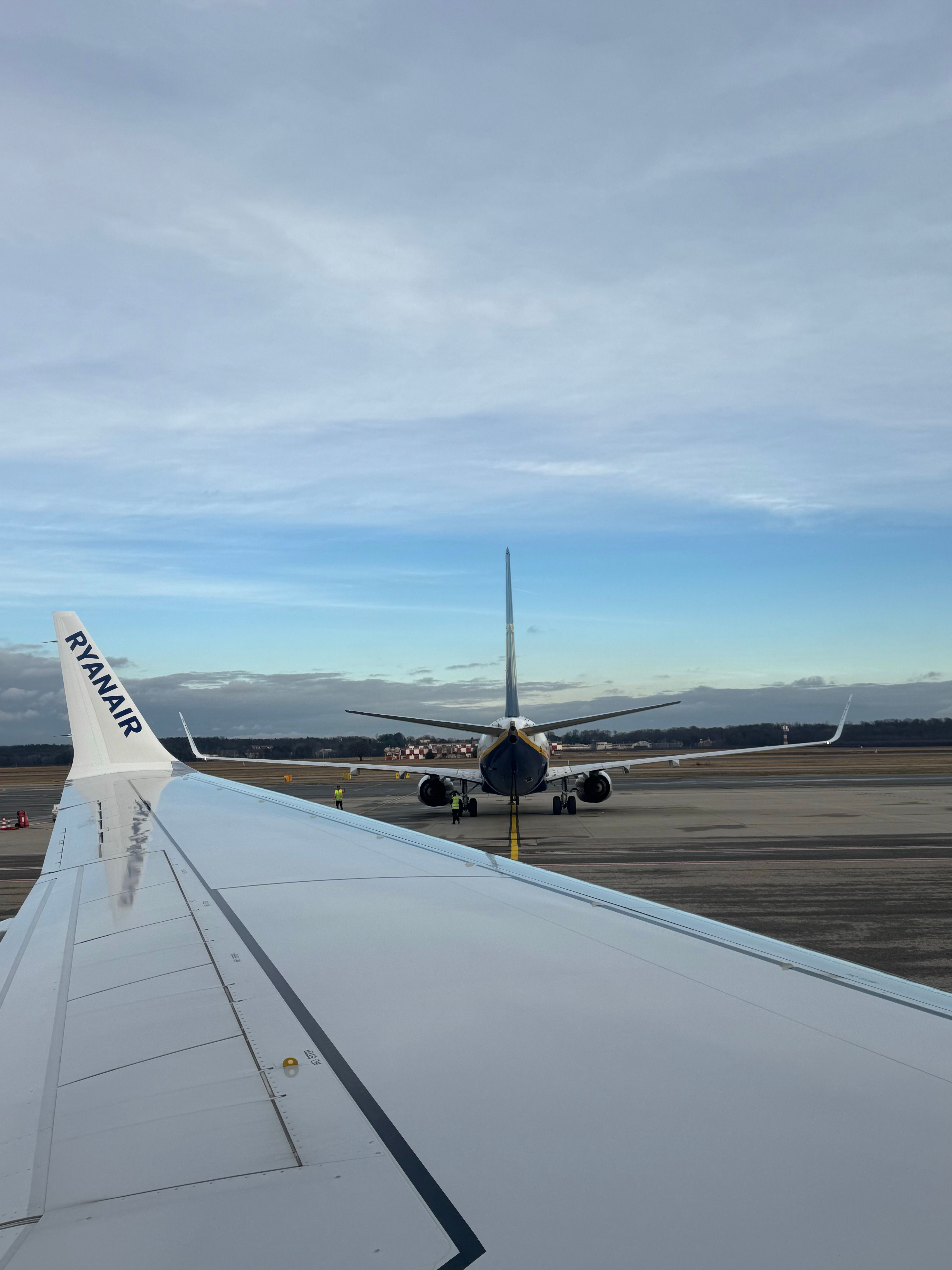 View from a plane's wing on a tarmac, showcasing another airplane ahead under clear skies.