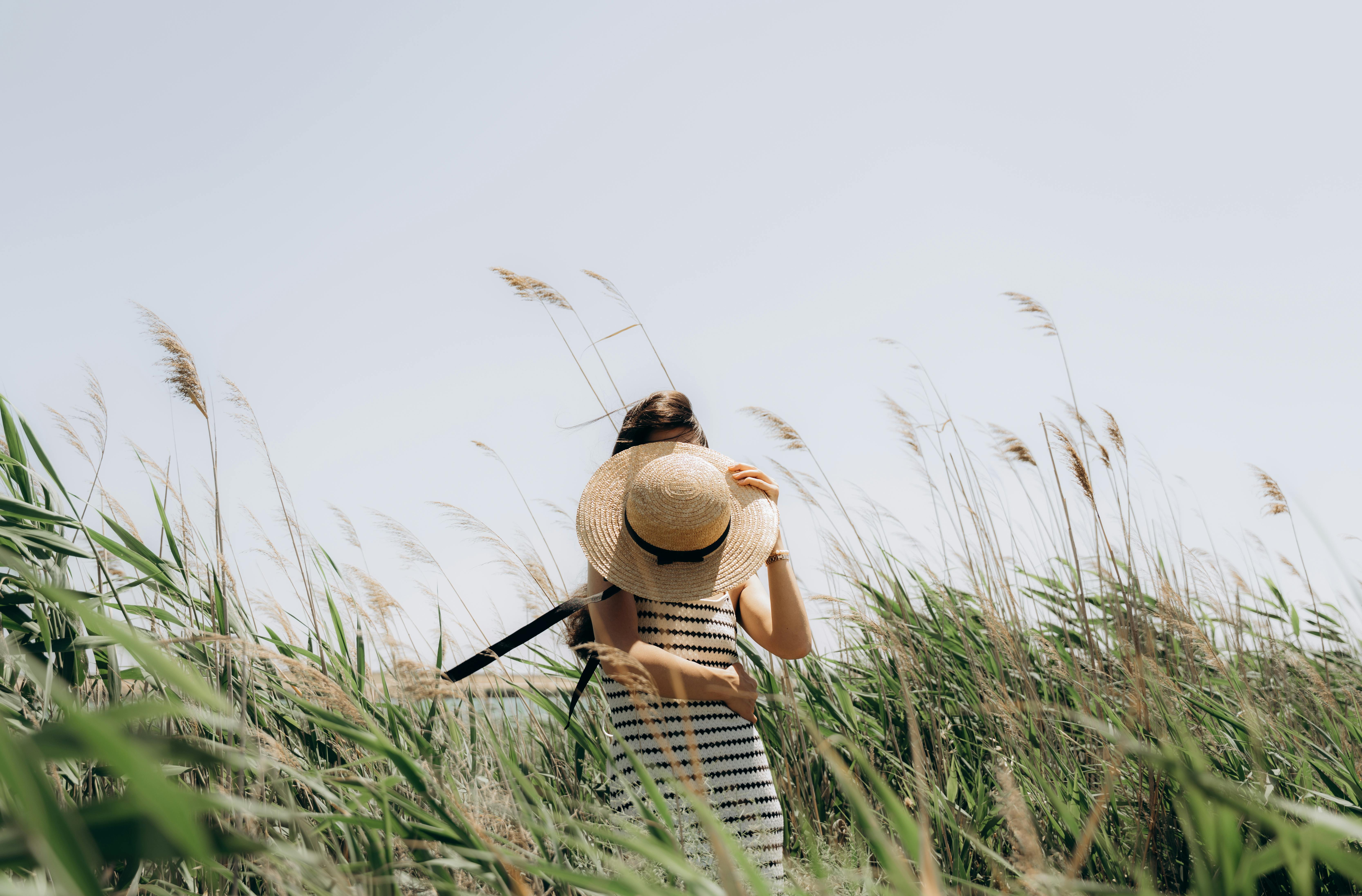 A woman with a sun hat and backpack stands amidst tall grass on a sunny summer day in Baku, Azerbaijan.
