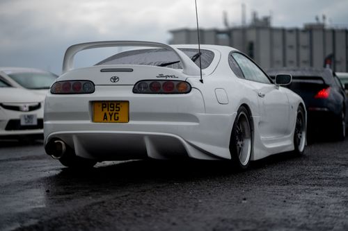 Free Rear view of a modified white Toyota Supra on a wet race track, showcasing its distinctive spoiler. Stock Photo