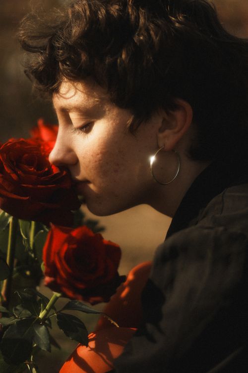 Free A young woman with short hair gently smells blossoming red roses outdoors. Stock Photo