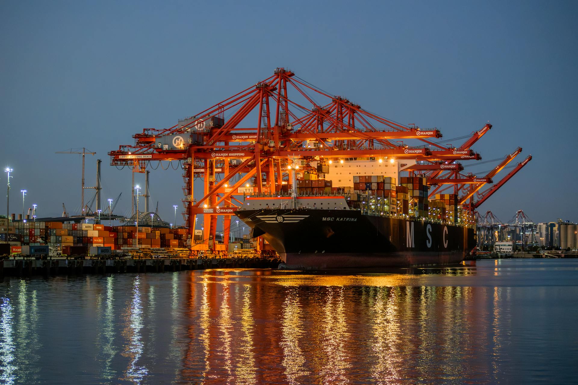 Cargo containers being loaded onto a ship at a bustling port, captured during twilight hours.