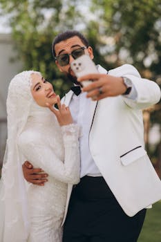 Bride and groom taking a selfie outdoors in elegant wedding attire.
