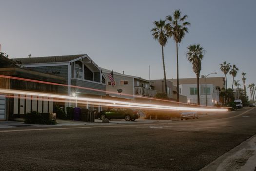 Palm-lined street with light trails from cars at twilight, showcasing modern coastal homes.