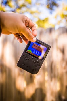 Hand holding a vintage handheld gaming console displaying Super Mario Bros against an outdoor blurred background.