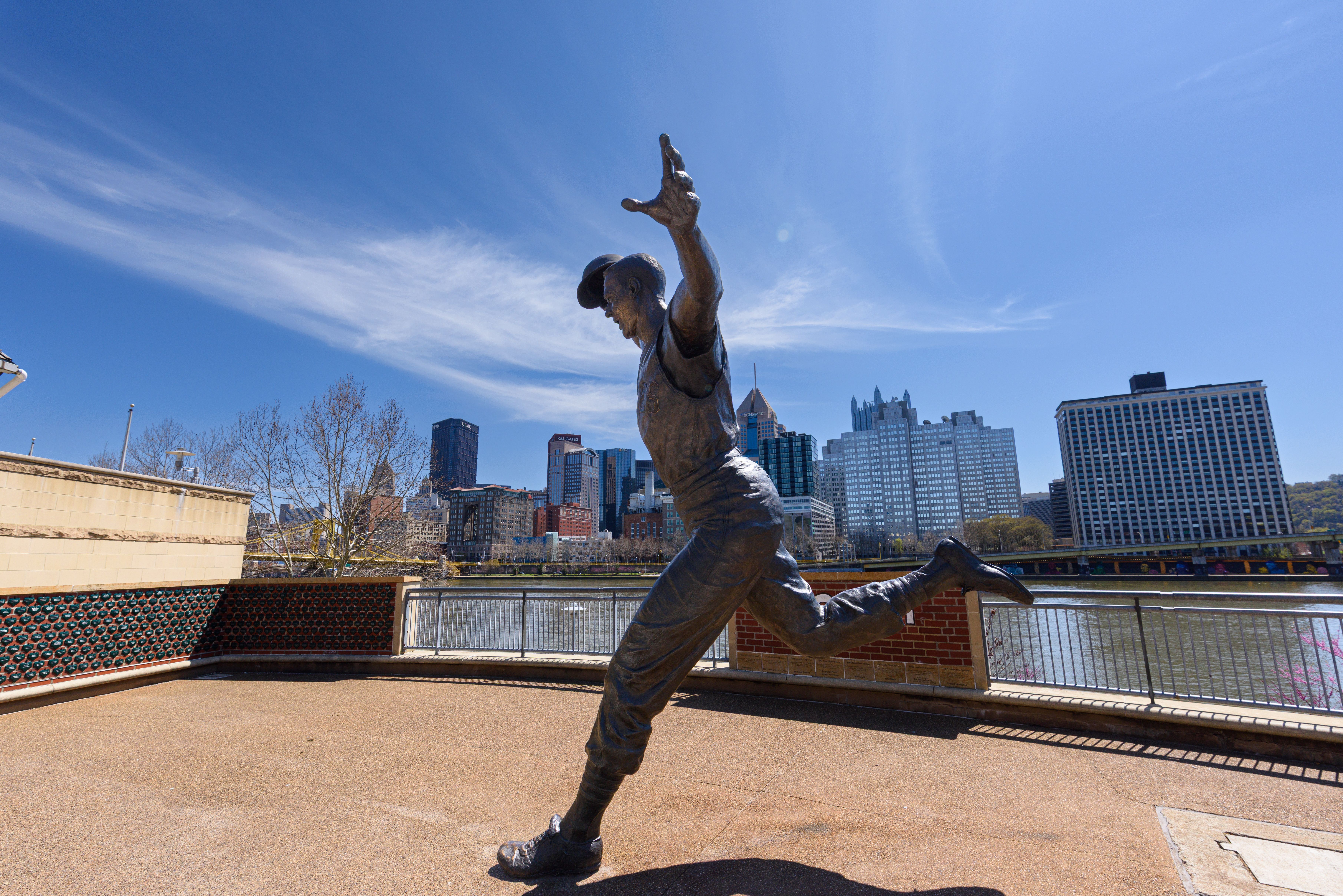 MLB photo featuring A striking statue of a baseball player set against a vibrant city skyline under a clear blue sky.