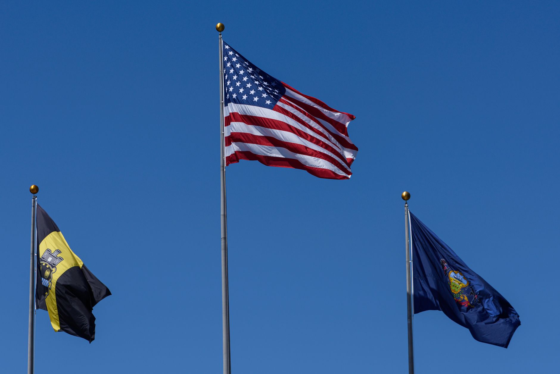 Three flags including the US flag waving against a clear blue sky.