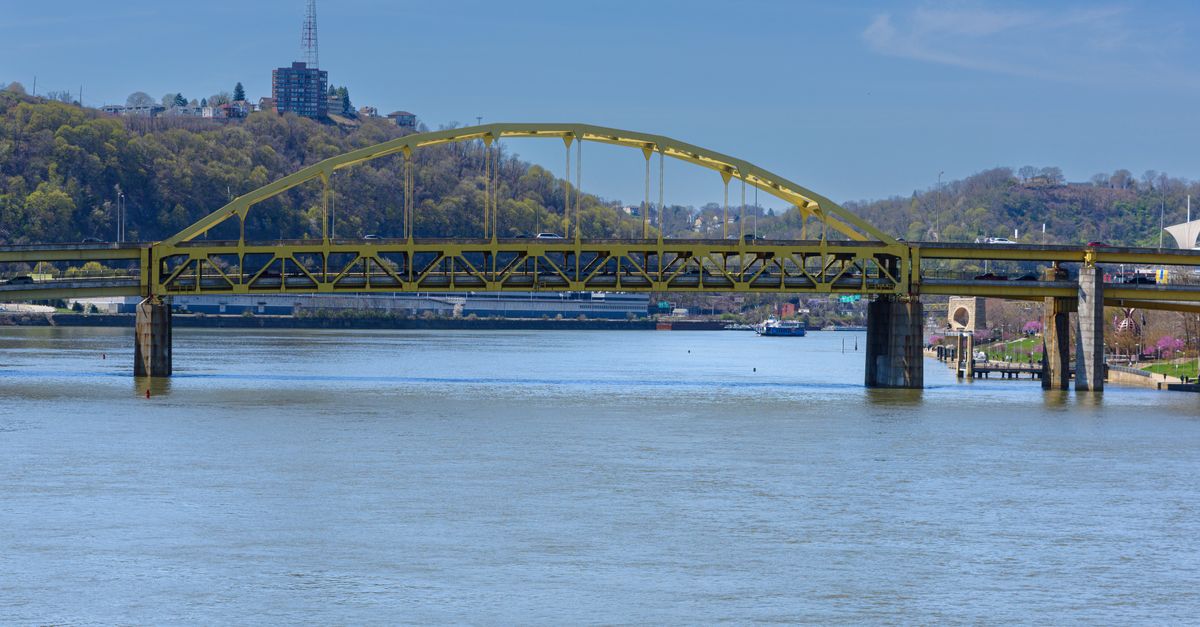 Yellow arch bridge over a river with lush greenery and a clear blue sky in a serene landscape.