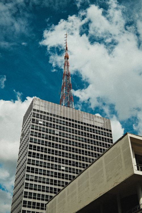 Free High-rise building with communication antenna against a vivid blue sky and clouds. Stock Photo