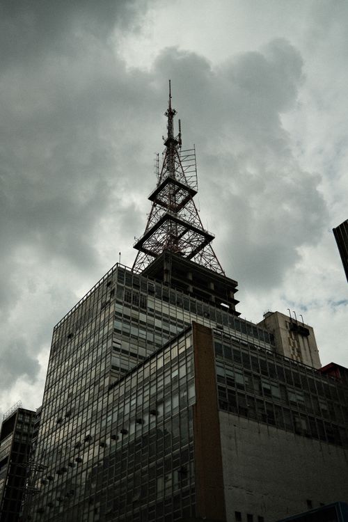 Free A modern skyscraper with a TV antenna under a dramatic cloudy sky, showcasing urban architecture. Stock Photo