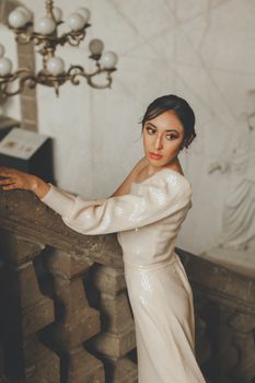 Sophisticated woman in a vintage gown poses on stairs in classic indoor setting.