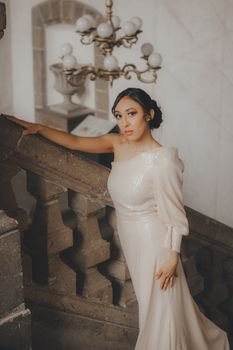 Woman in elegant dress poses on vintage staircase indoors, soft lighting.