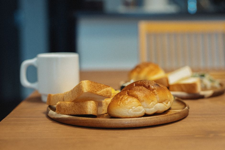 木のテーブルに日本のパンとコーヒーを並べた温かい朝のセットアップ。
