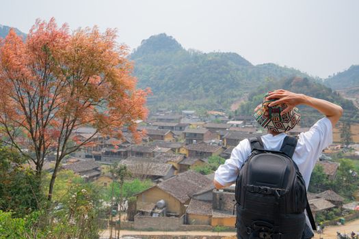 Traveler with backpack enjoys view of a picturesque mountain village amid vibrant autumn foliage.