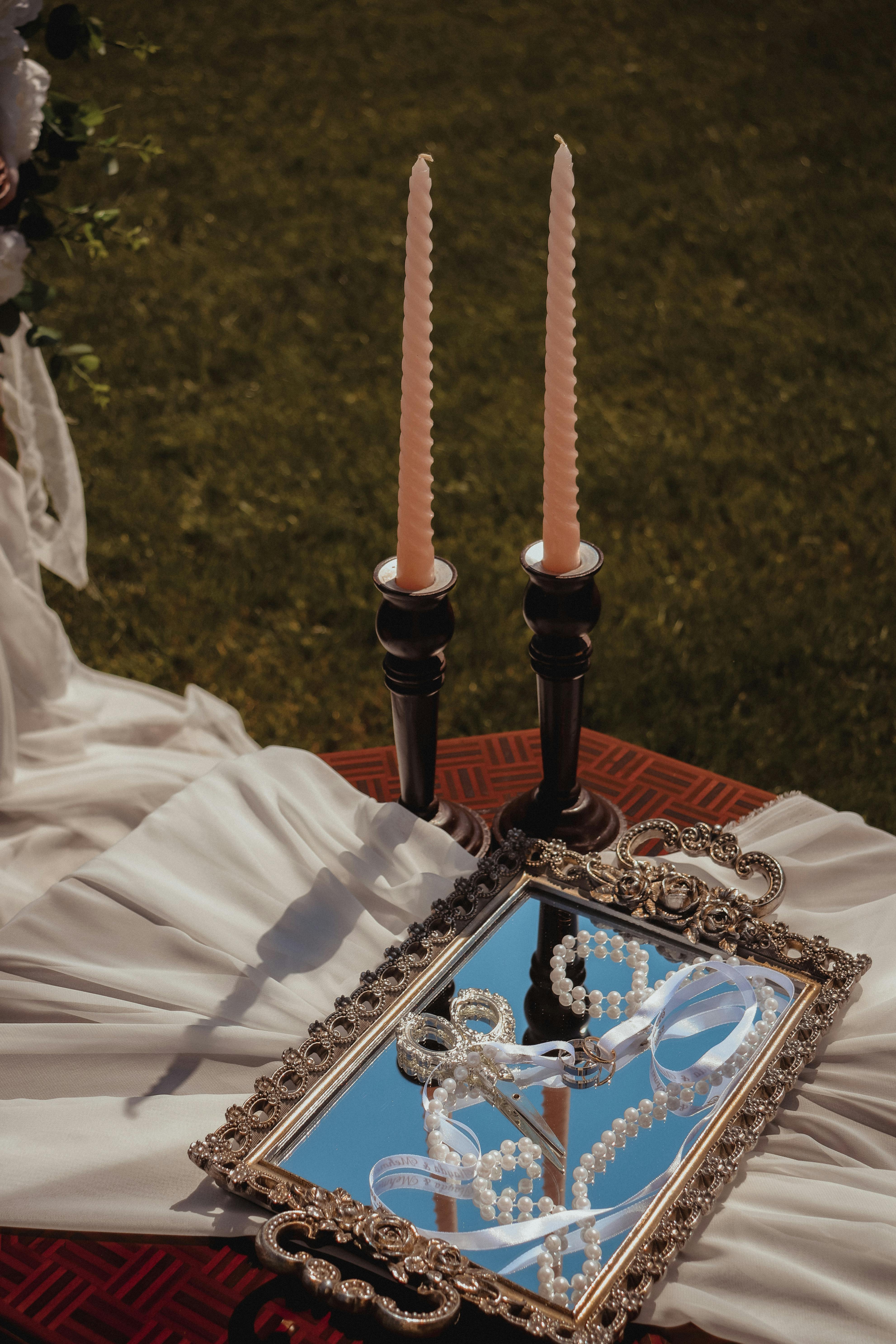 Romantic outdoor wedding decor with candles, mirror, and pearls on a white draped table.