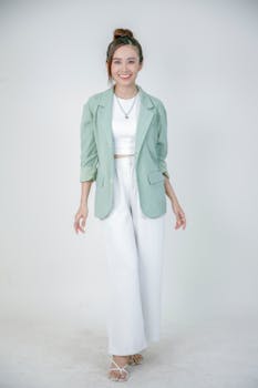 Stylish young woman in a pastel green blazer and white outfit, posing confidently in a minimalistic setting.