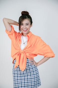 Fashionable woman in bright orange top and blue patterned skirt, posing happily indoors.