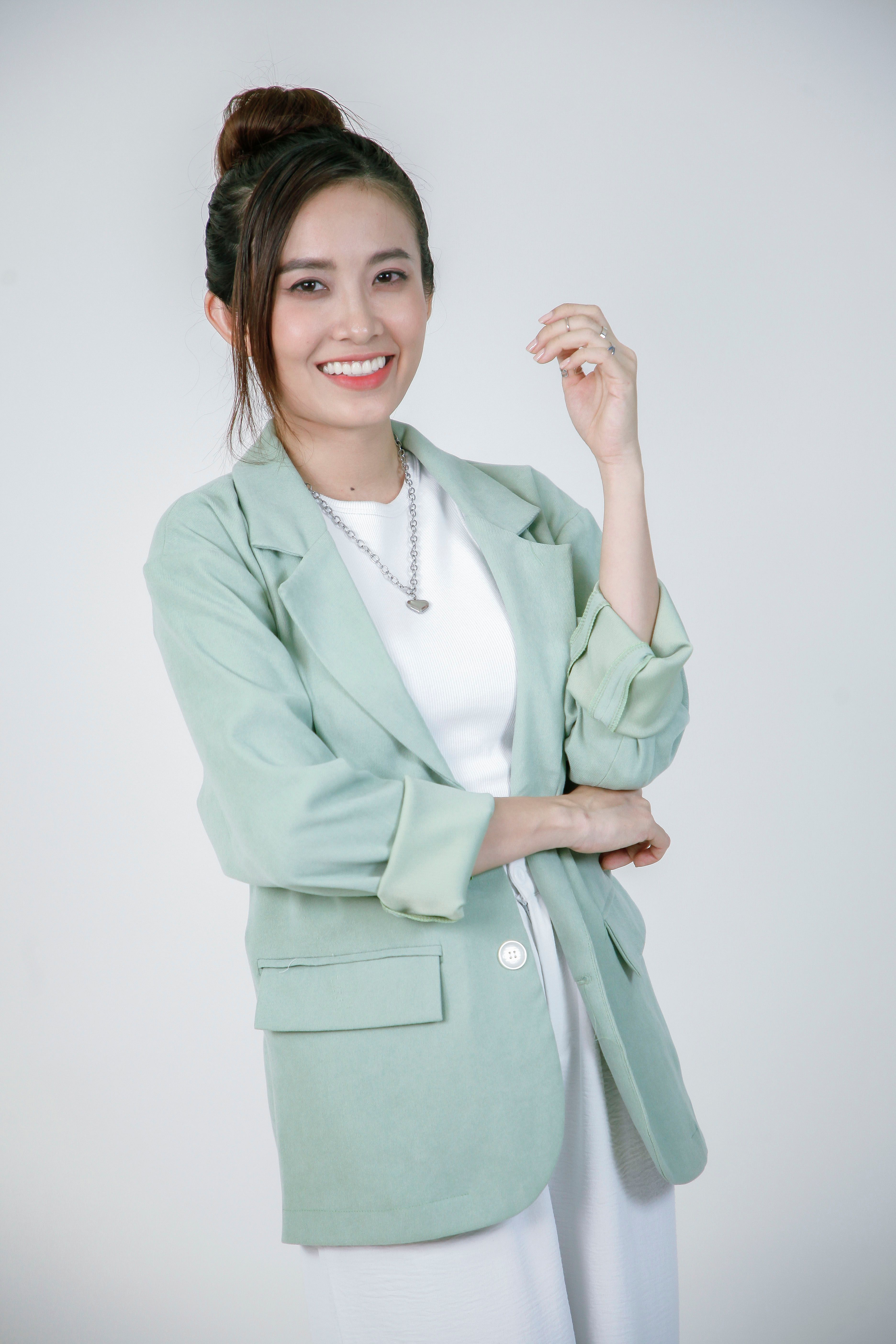Portrait of a smiling woman wearing a chic green blazer and white outfit.
