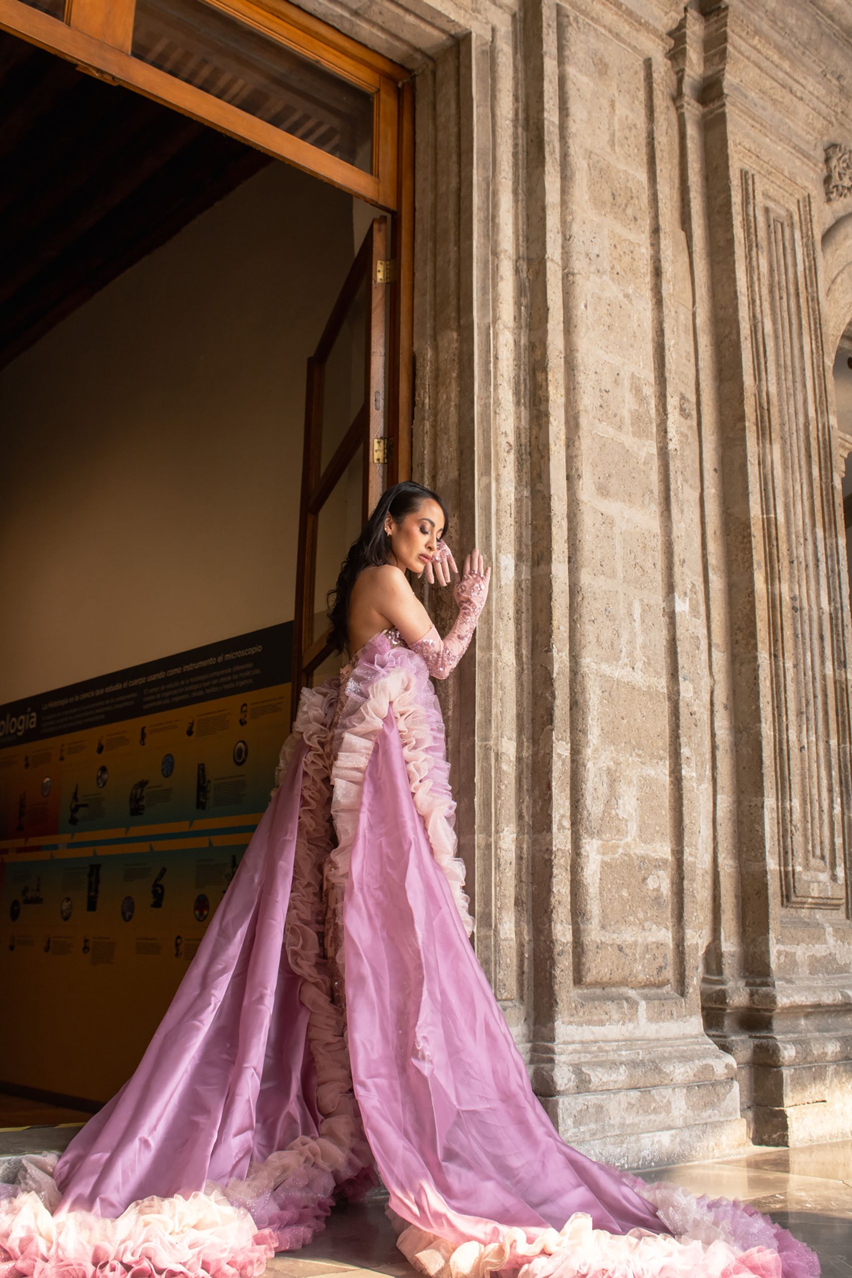 A woman in a pink gown poses gracefully by a historic building in Mexico City.