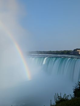Captivating view of Niagara Falls with a vibrant rainbow on a clear day.