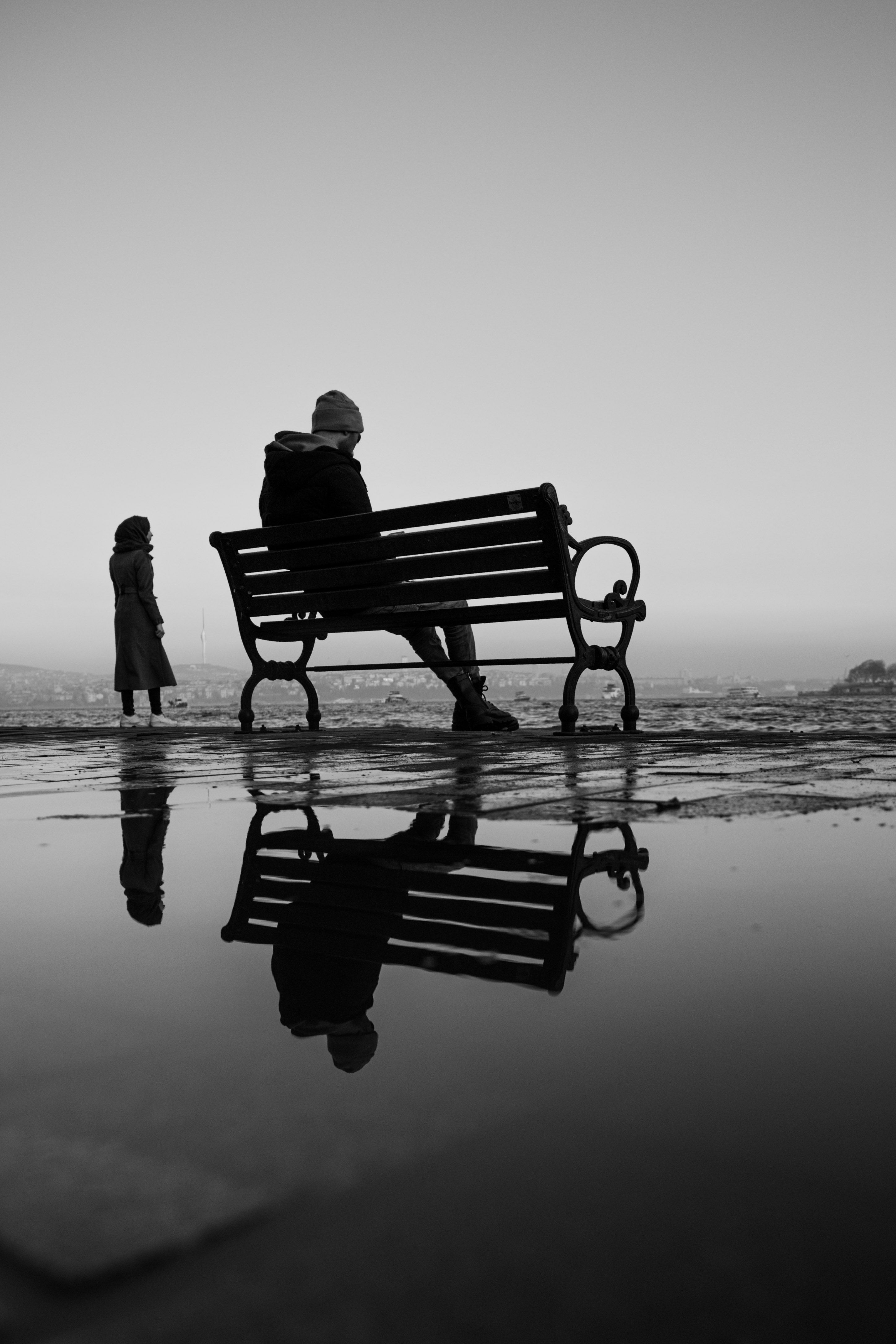 Dramatic silhouette of two people near a bench reflecting in a puddle in Istanbul.